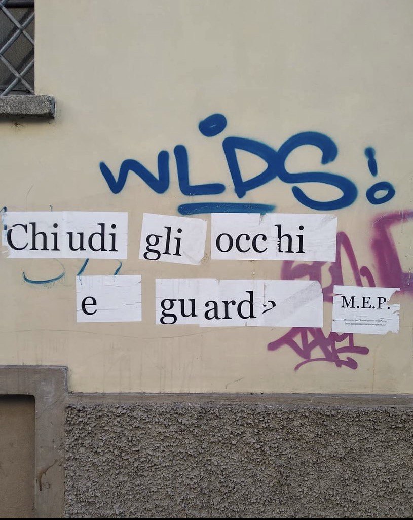 Un muro di una casa di Milano con la scritta Chiudi gli occhi e guarda